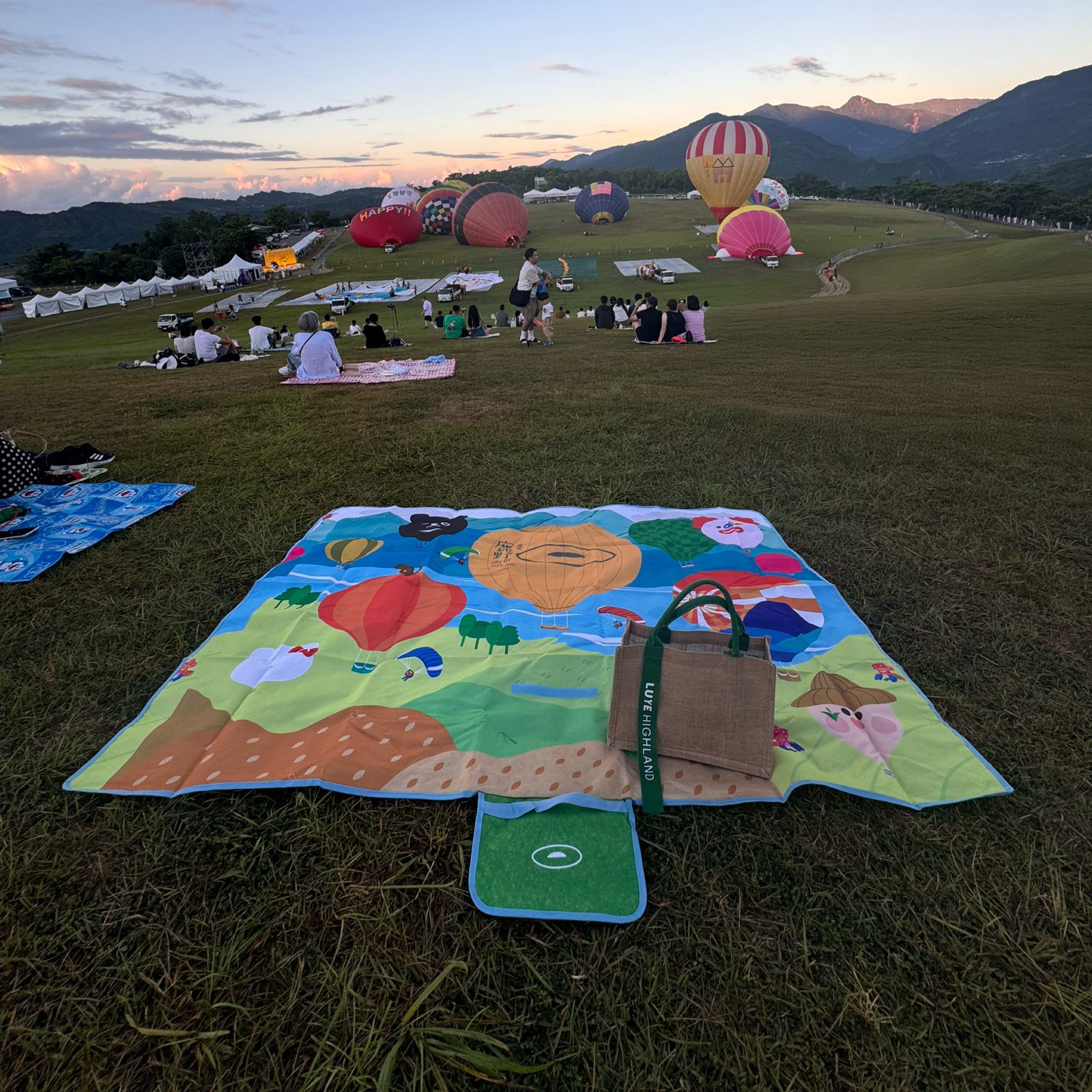 野餐墊鋪展於鹿野高台熱氣球嘉年華現場，遠方多顆熱氣球升空