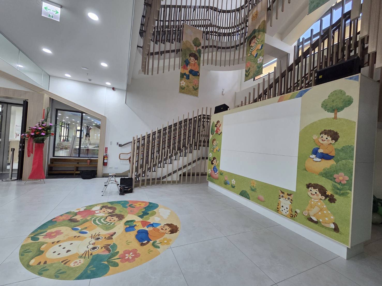 苗栗親子館暨托嬰中心大廳全景，入口地貼、投影牆與天井旗幟一次到位